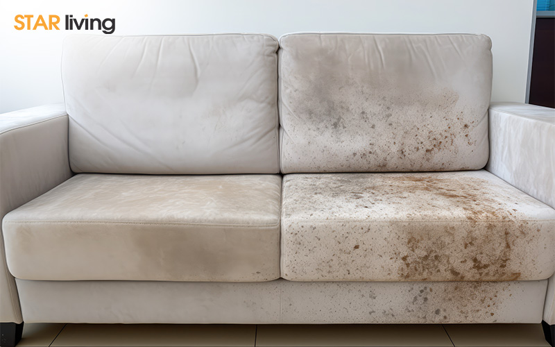 Close-up of a white fabric sofa with visible mould and dirt stains on the right side, highlighting poor indoor air quality and hygiene.