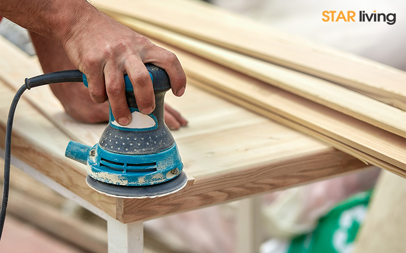 hand using a blue electric sander on a wooden surface