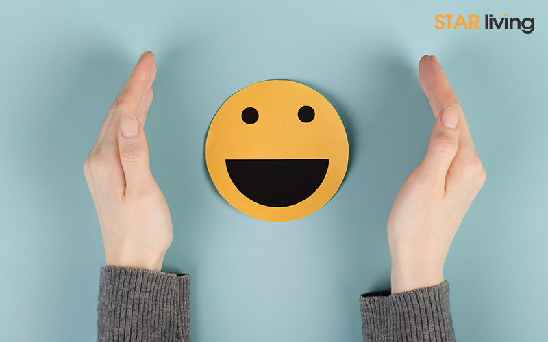 hands in gray sleeves surround a yellow smiley face on a blue background
